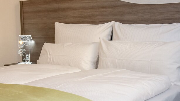 A neatly made bed with white linens and a wooden headboard. - Rhöner Ferienwohnung (Dermbach)