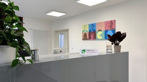 A reception area with a glass desk, a potted plant, a sign for EMPFANG, and a colorful artwork on the wall. - Rhöner Ferienwohnung (Dermbach)