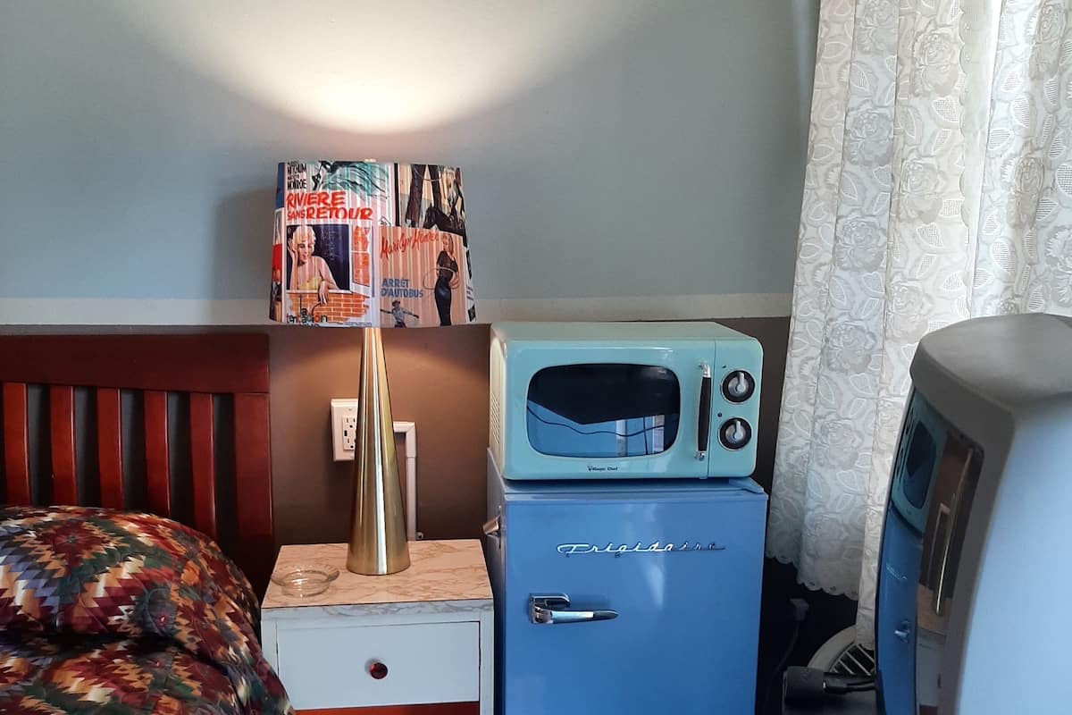 A hotel room with a bed, a small desk with a lamp, a microwave, a television, and a minibar.