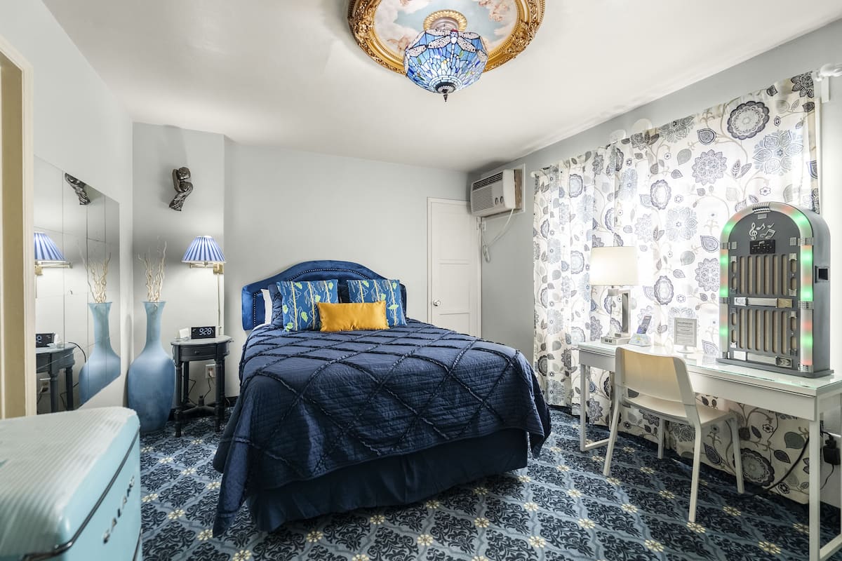 A hotel room with a bed, a desk, a chair, a lamp, and a decorative ceiling light.