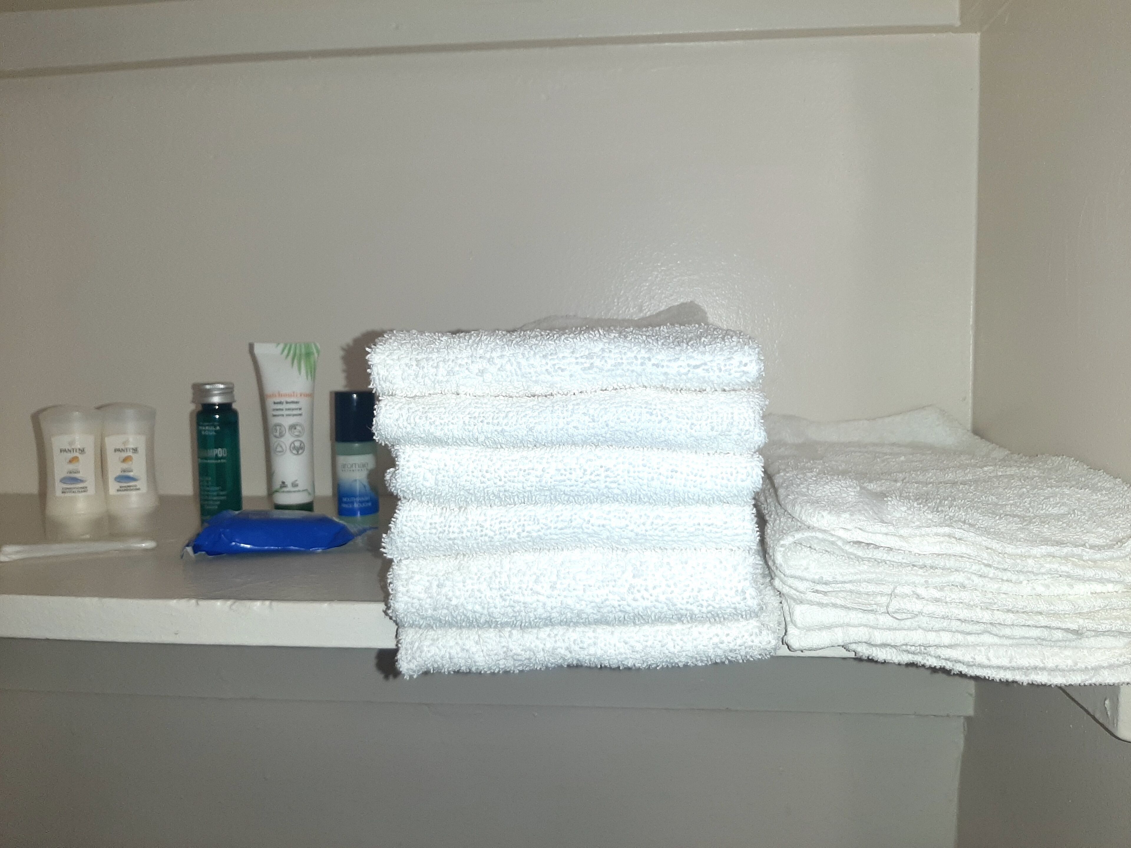 A bathroom with a stack of white towels, a blue soap dish, and various toiletries on a shelf.
