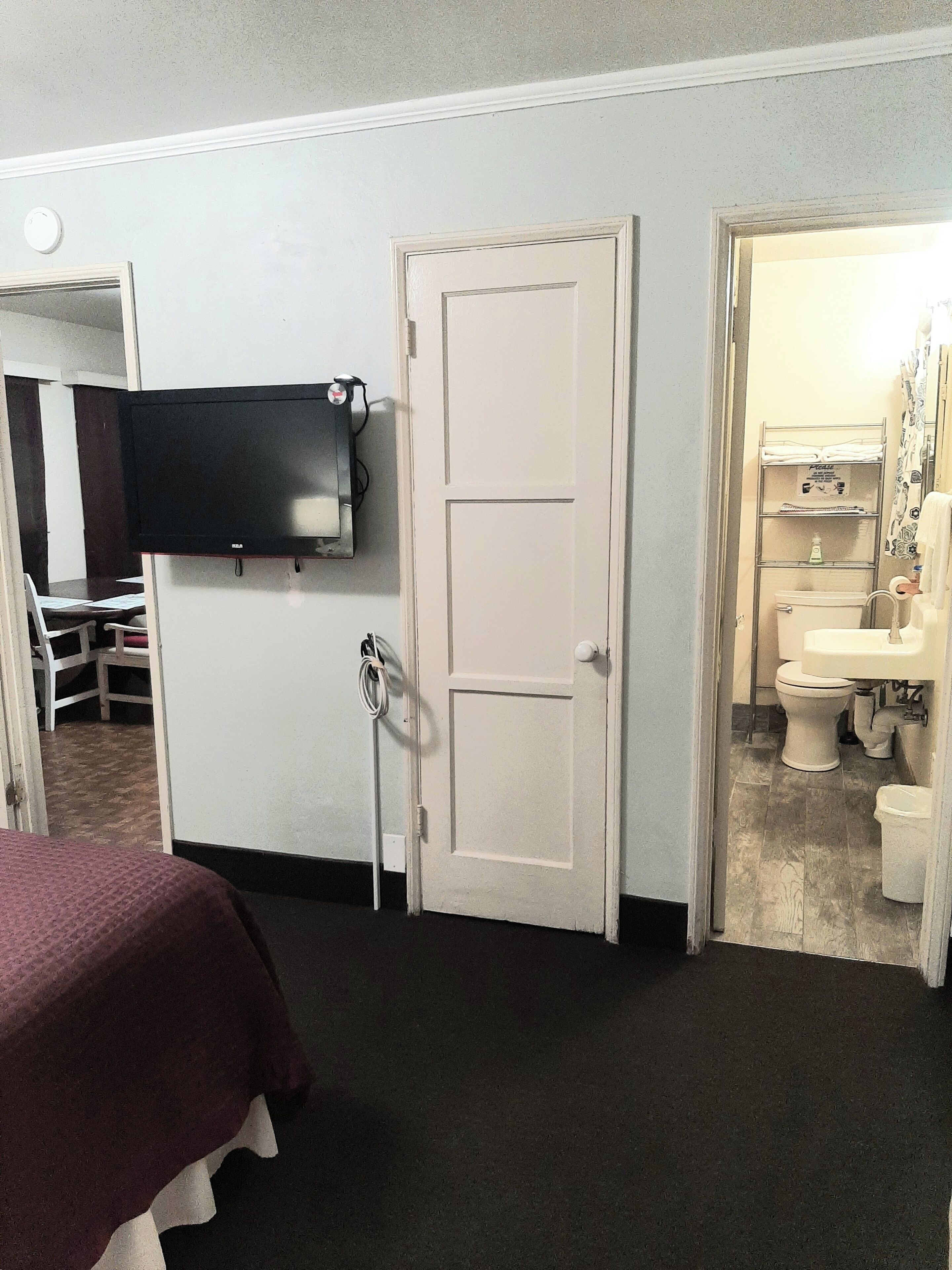 A hotel room with a bed, a television mounted on the wall, a door leading to a bathroom, and a small table with chairs.