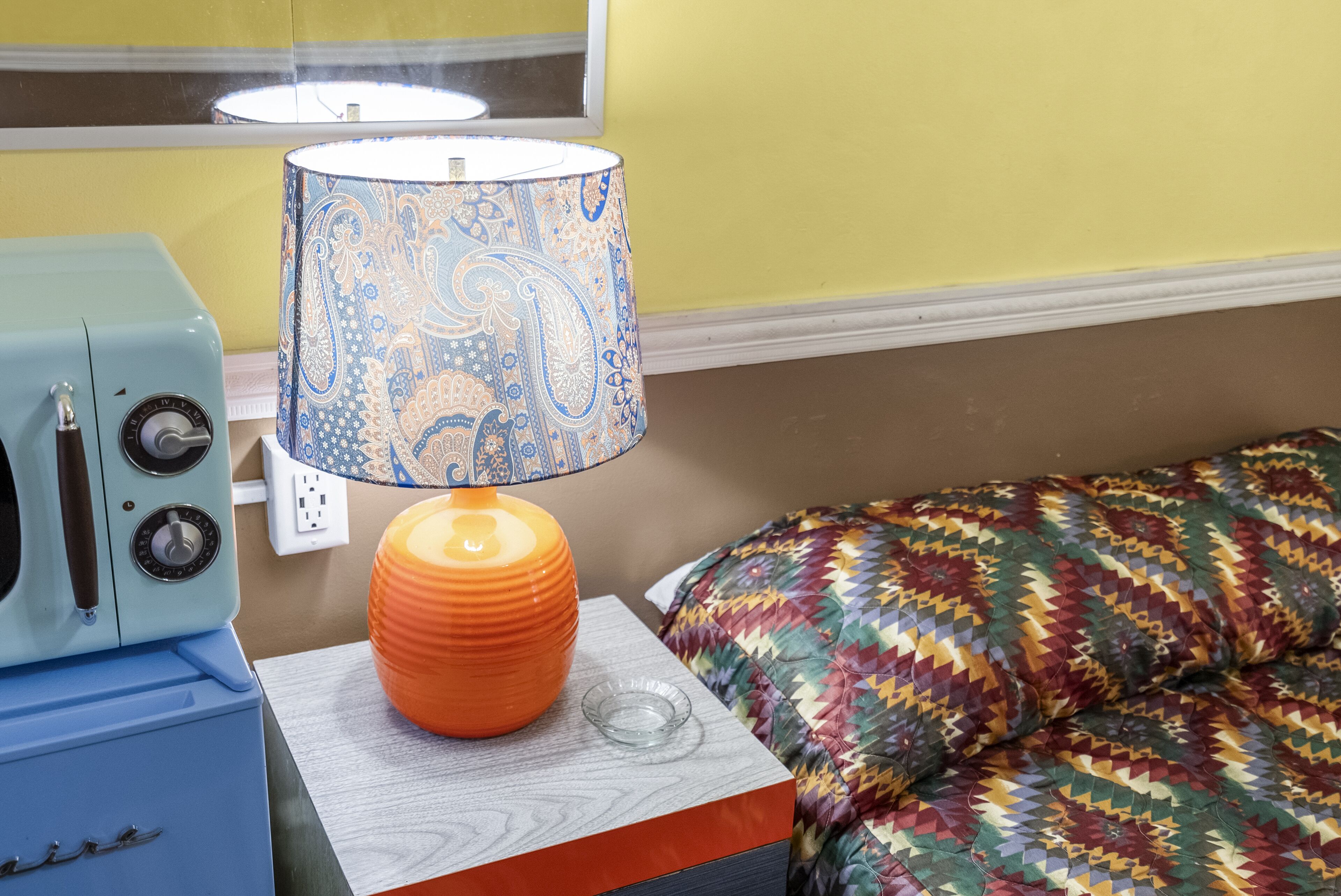 A room with a patterned lamp, a vintage radio, and a colorful bedspread.