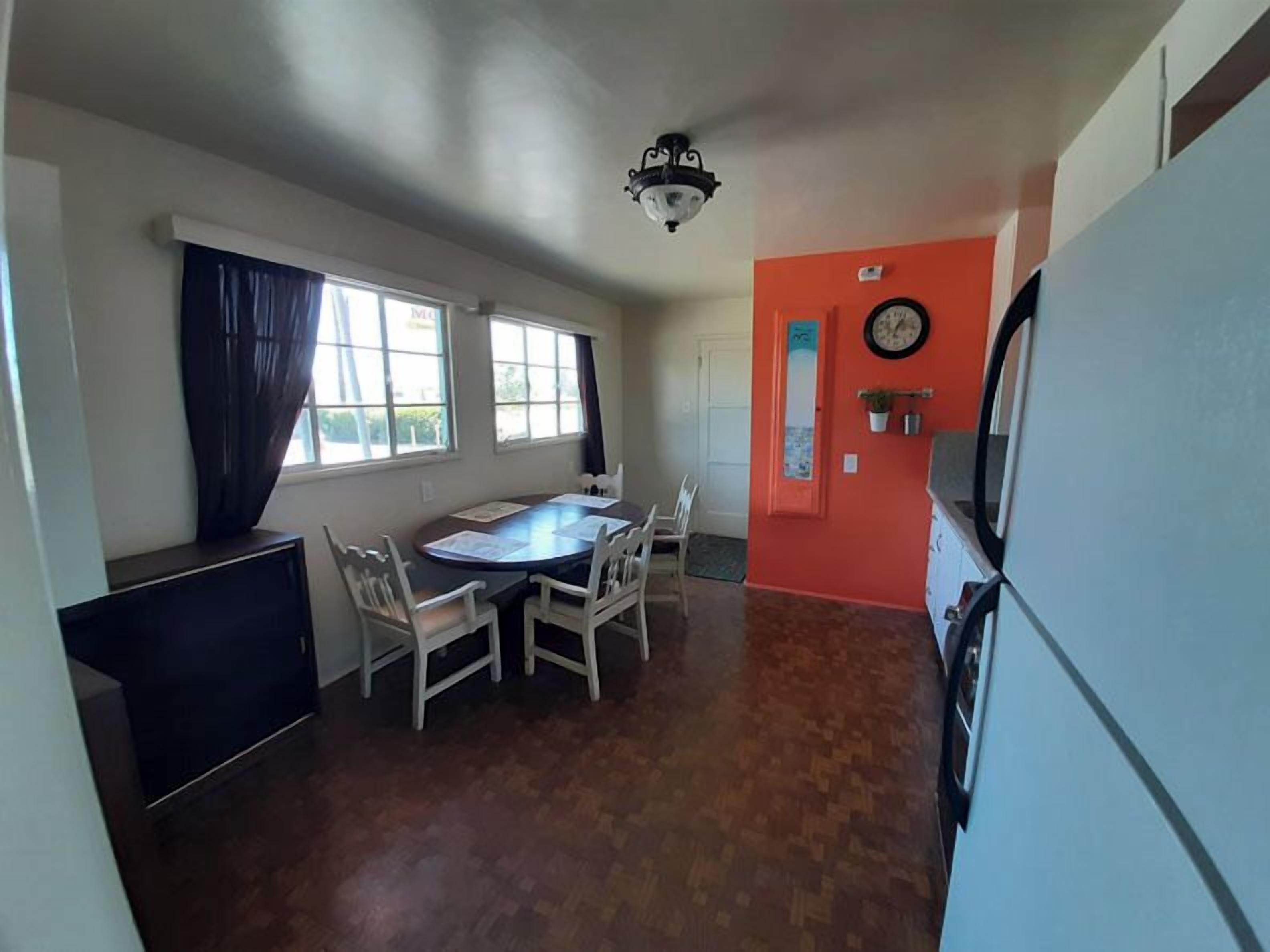 A compact kitchen with a dining table and chairs, a refrigerator, and a clock on the wall.