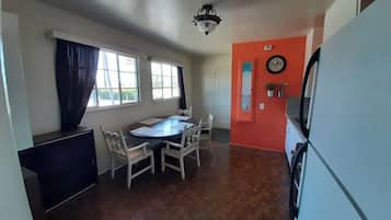 A compact kitchen with a dining table and chairs, a refrigerator, and a clock on the wall.