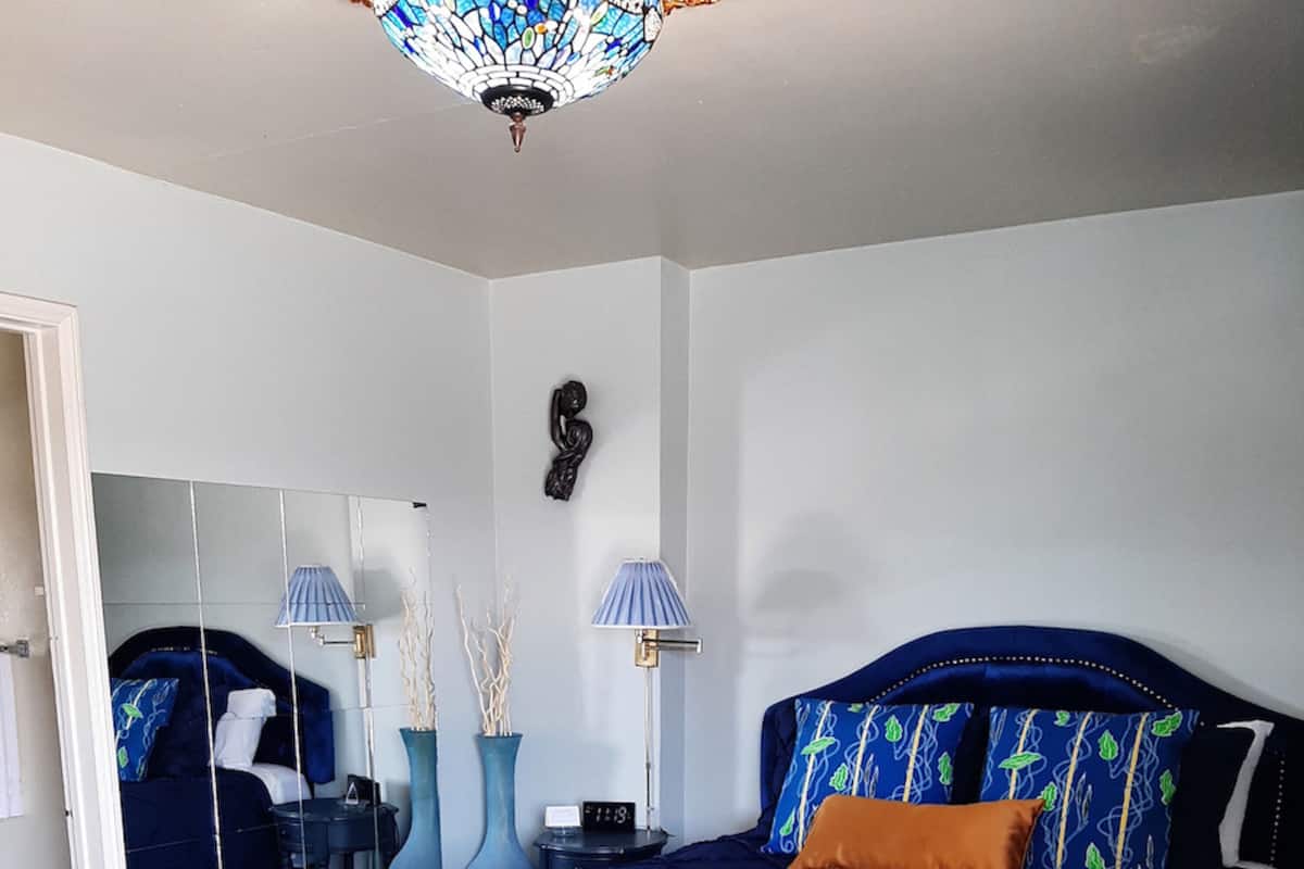 A bedroom with a large bed, a mirror, two wall-mounted lamps, and a decorative sculpture.
