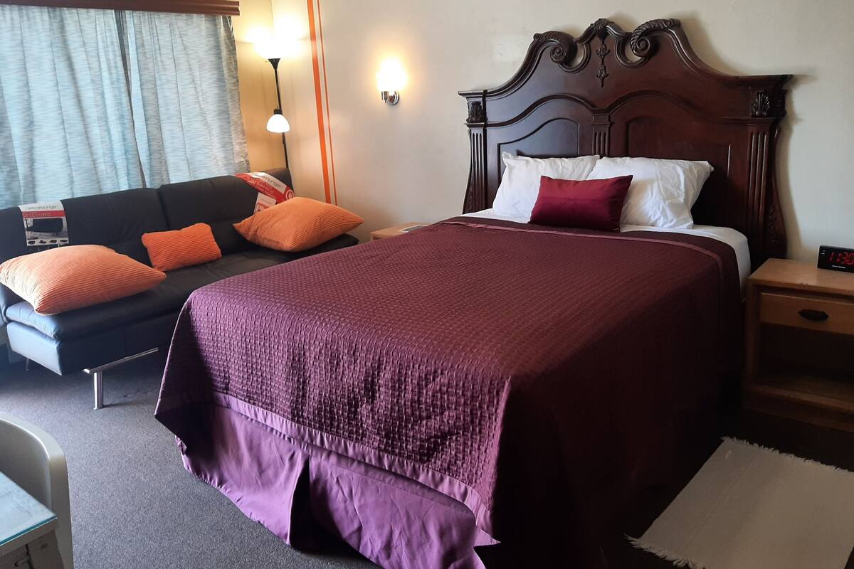 A hotel room with a large bed, a sofa, and a nightstand.