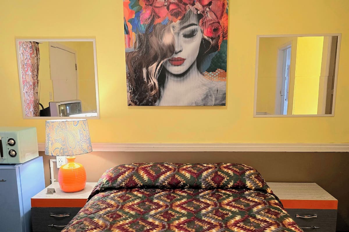 A room with a bed, a desk, a lamp, and a painting on the wall.