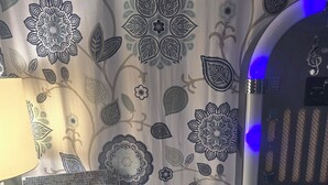 A room with a patterned wallpaper, a framed photograph, a CD, a small table with a lamp, and a door with a blue light. - Harry's Man Cave: The New Star Motel Experience (Moreno Valley)