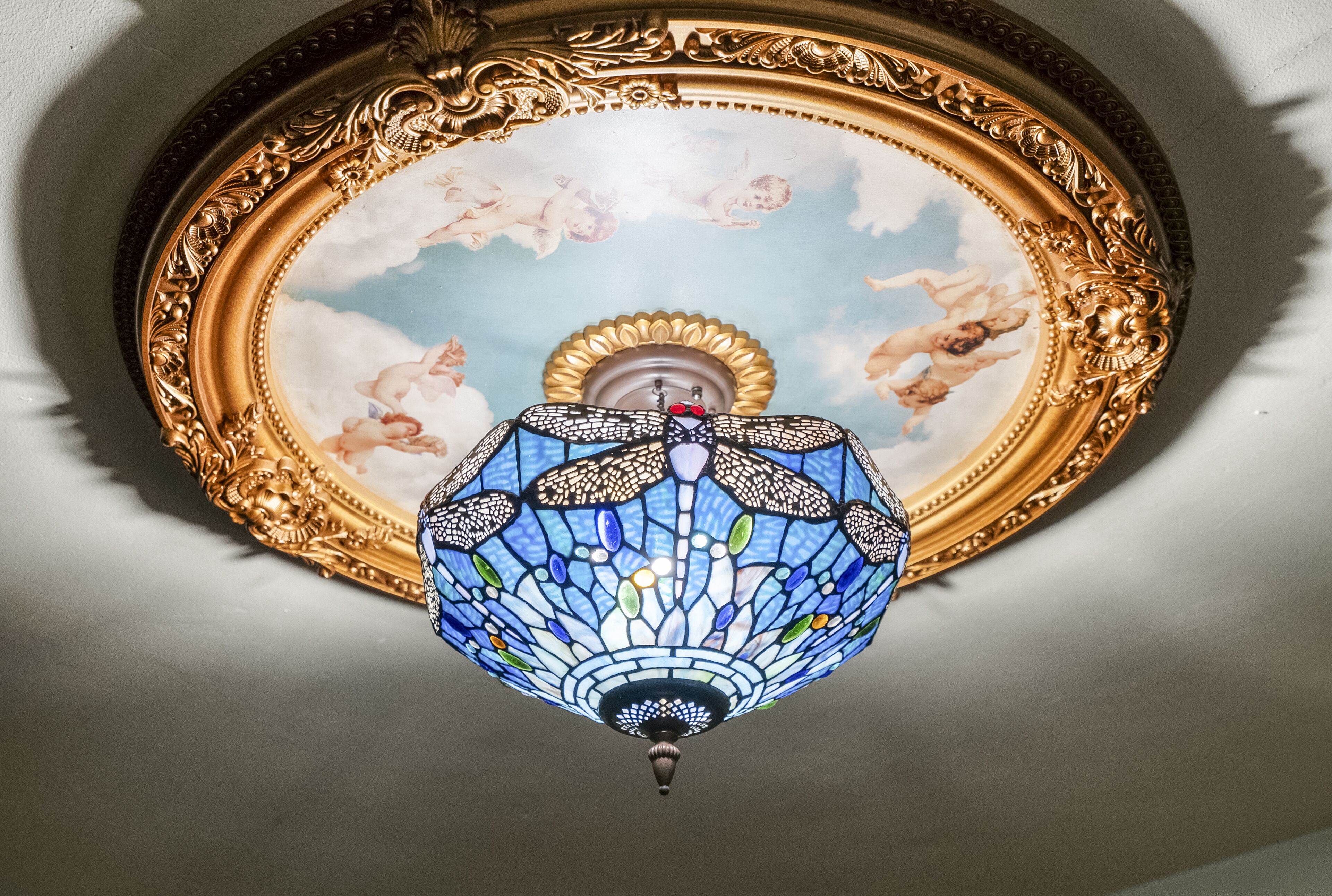 A ceiling with a decorative stained glass light fixture and a framed painting.