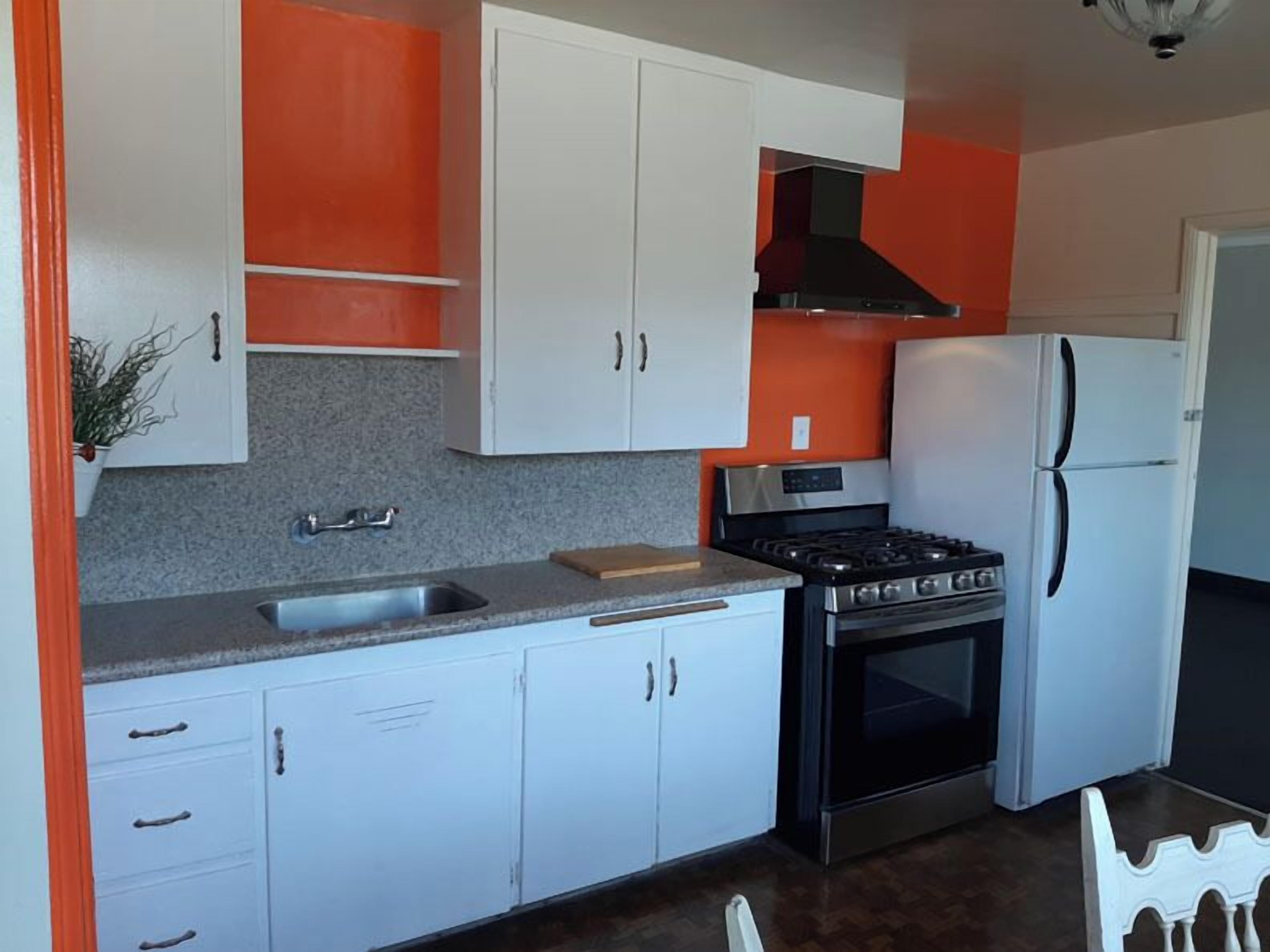 A kitchen with white cabinets, a stainless steel sink, a stove, and a refrigerator.