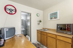 Una cocina compacta con mostrador de madera, un microondas antiguo, un lavamanos pequeño y una puerta que da a un baño.