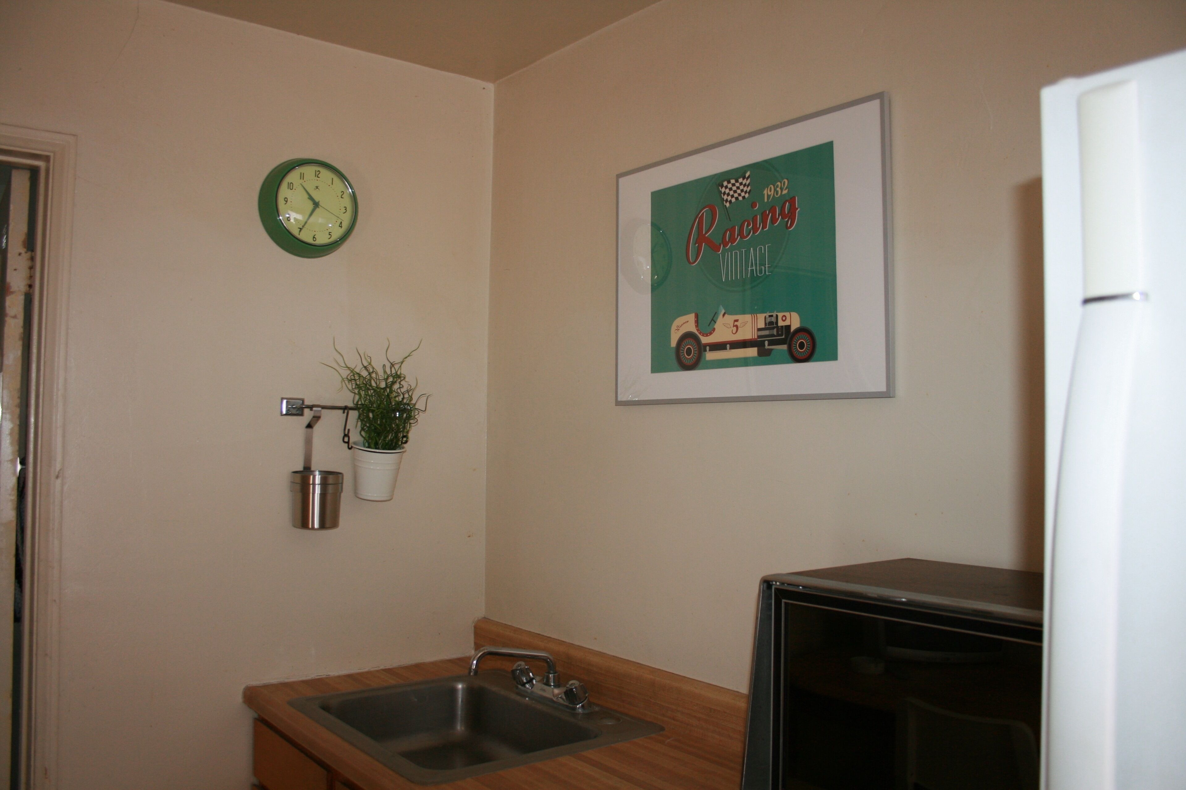 Una cucina con un lavandino, un orologio, un poster vintage di una gara automobilistica incorniciato e una pianta in vaso.