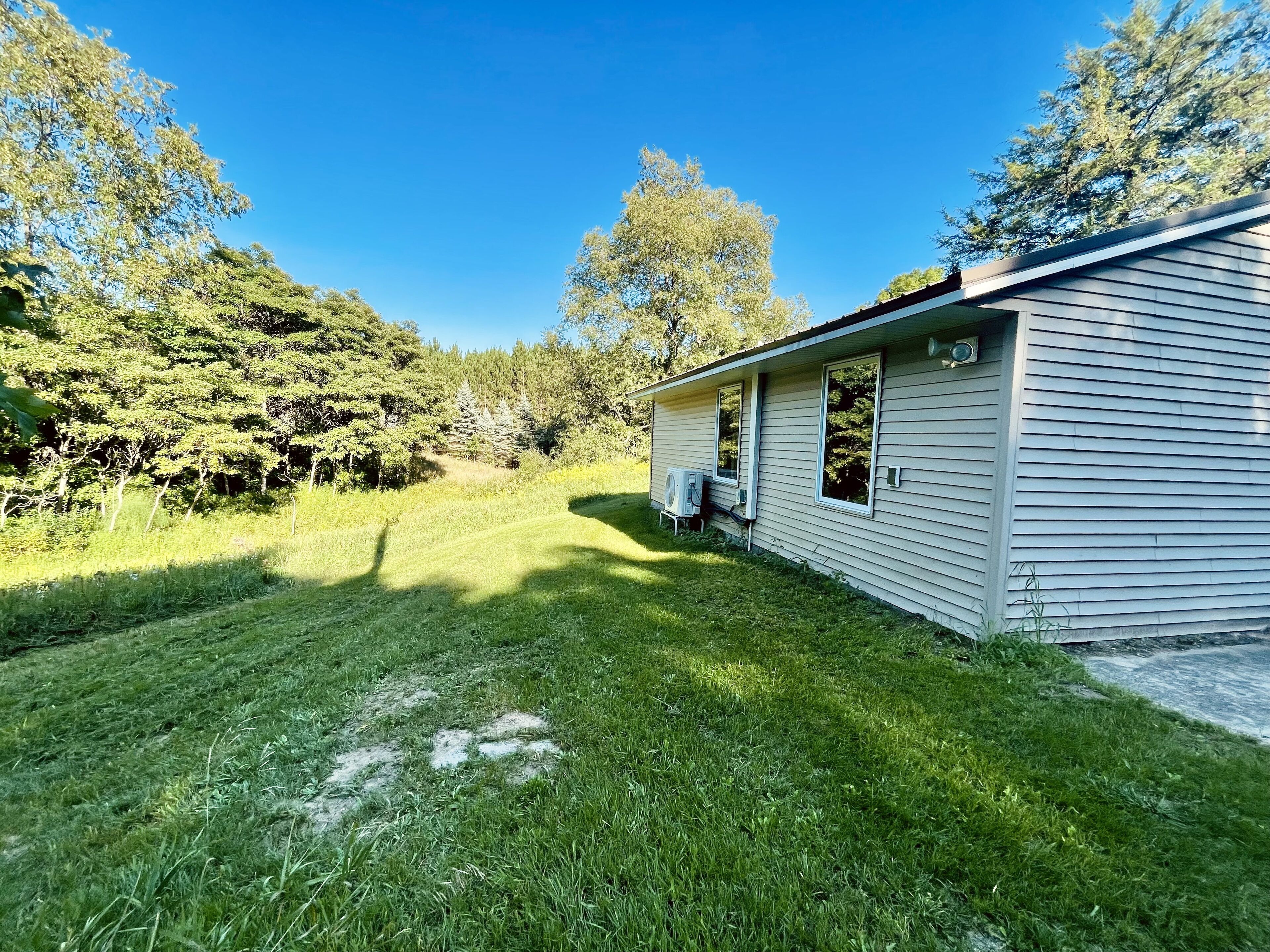 A single-story mobile home with a small porch, surrounded by a grassy yard and dense trees.