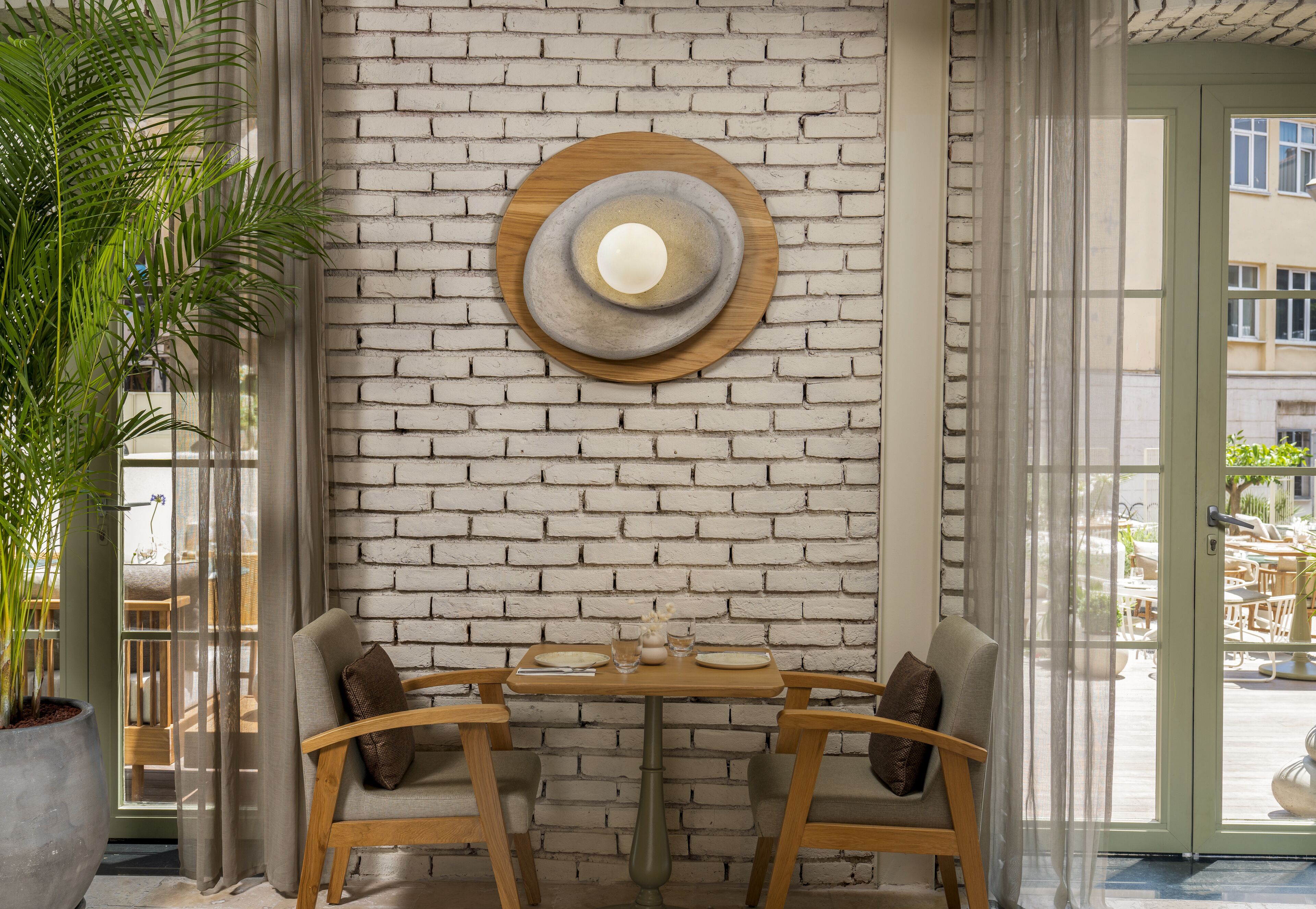 Un comedor con pared de ladrillo, una mesa redonda de madera, dos sillas y una planta en maceta.