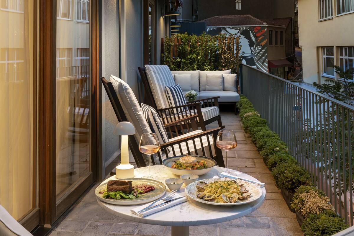 An outdoor dining area with a table set for two, a cushioned bench, and a view of a tower in the background.