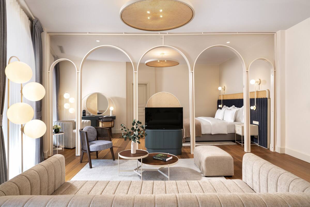 A modern hotel room with a sofa, armchair, round coffee table, and a TV.