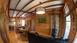A cozy cabin interior with a wooden floor, a black leather sofa, a dining table with chairs, a kitchen area, and a stone fireplace. - Ecolodge And Wines with native nature, where Chilean wine was born. (Guarilihue)