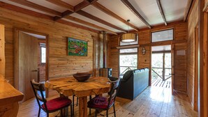 A wooden interior with a round table, chairs, a sofa, and a large window. - Ecolodge And Wines with native nature, where Chilean wine was born. (Guarilihue)