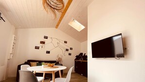 A modern living space with a dining area, a sofa, a TV mounted on the wall, and a ceiling with wooden beams.