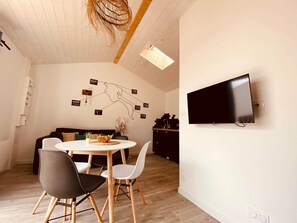 Um espaço de estar moderno com área de jantar, sofá, TV na parede e teto com vigas de madeira.