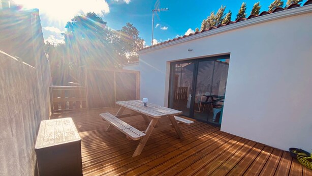 A wooden deck with a picnic table and a sliding glass door leading to a covered area.
