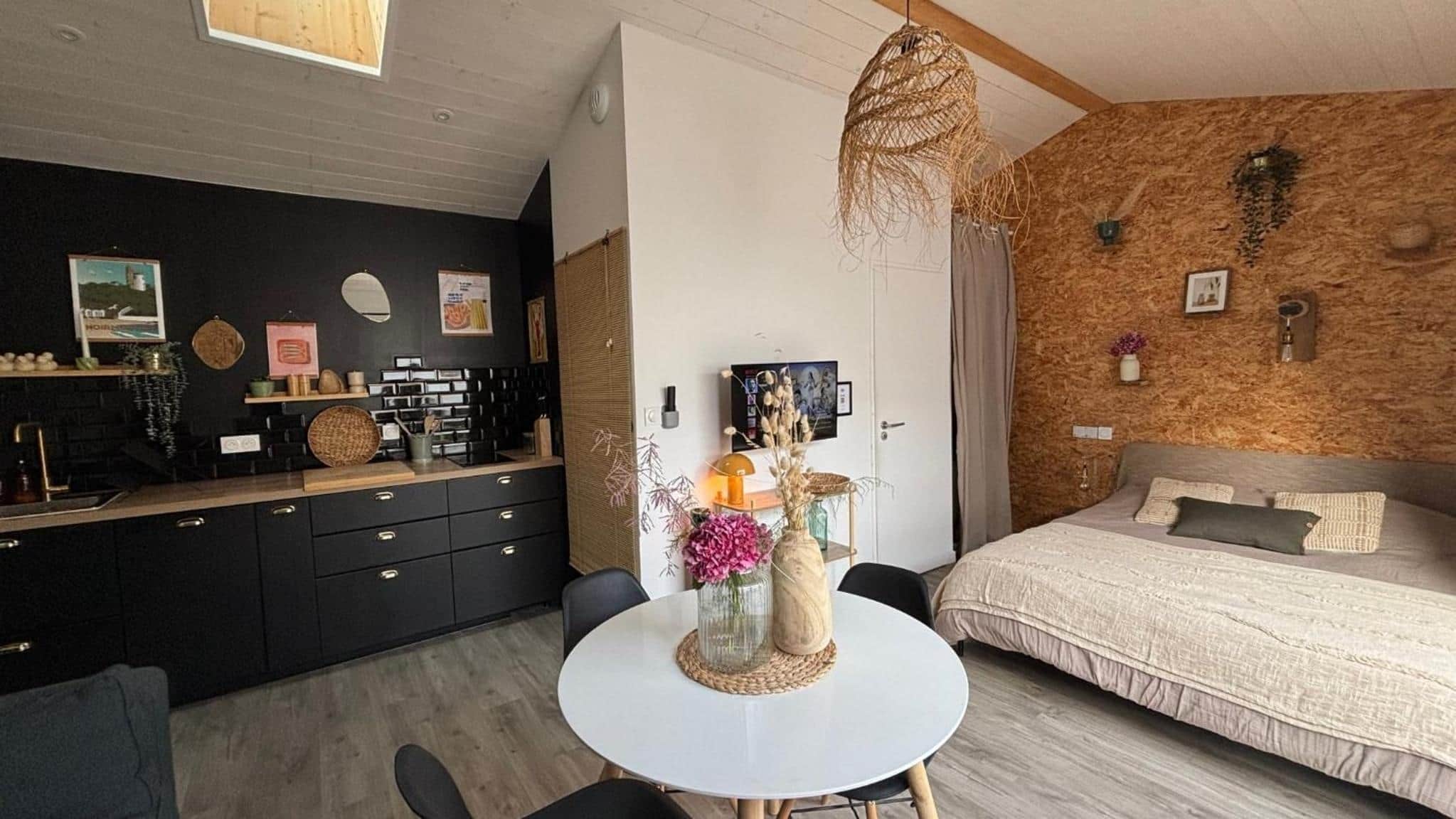 Une chambre moderne avec un grand lit, un coin repas avec une table ronde et une cuisine avec des meubles noirs.