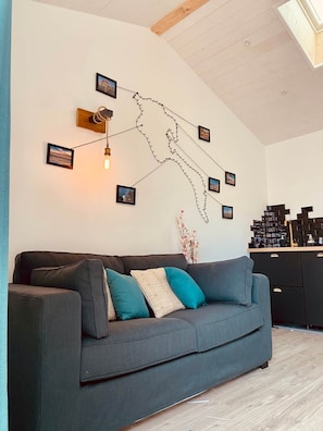 Uma sala de estar moderna com um sofá cinzento, almofadas verde-água e uma luminária fixada na parede.