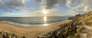 A beach with a rocky shoreline, a clear sky, and the sun setting over the horizon.