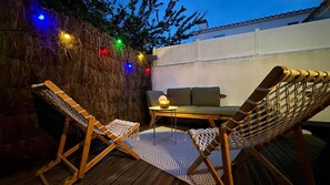 An outdoor seating area with two wooden chairs and a table, surrounded by a wall with colorful string lights.