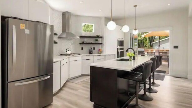 A modern kitchen with stainless steel appliances, a central island with bar stools, pendant lighting, and a view of the outdoors.