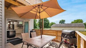 An outdoor deck with a table and chairs, a barbecue grill, and a large umbrella.