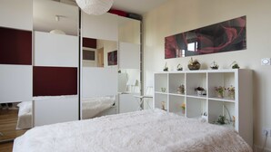 A bedroom with a large fluffy bed, a white wardrobe, a desk, and a mirror.