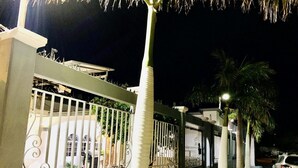 A gated residential area at night with a paved walkway, palm trees, and parked vehicles.
