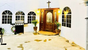A courtyard with a wooden door, a grill, and potted plants.