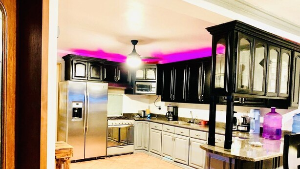 A kitchen with dark cabinets, stainless steel appliances, and a pink ceiling light.