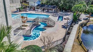 Zona de piscina con una piscina pequeña, una piscina más grande y un jacuzzi. Hay sillas de descanso y una zona de estar cubierta.