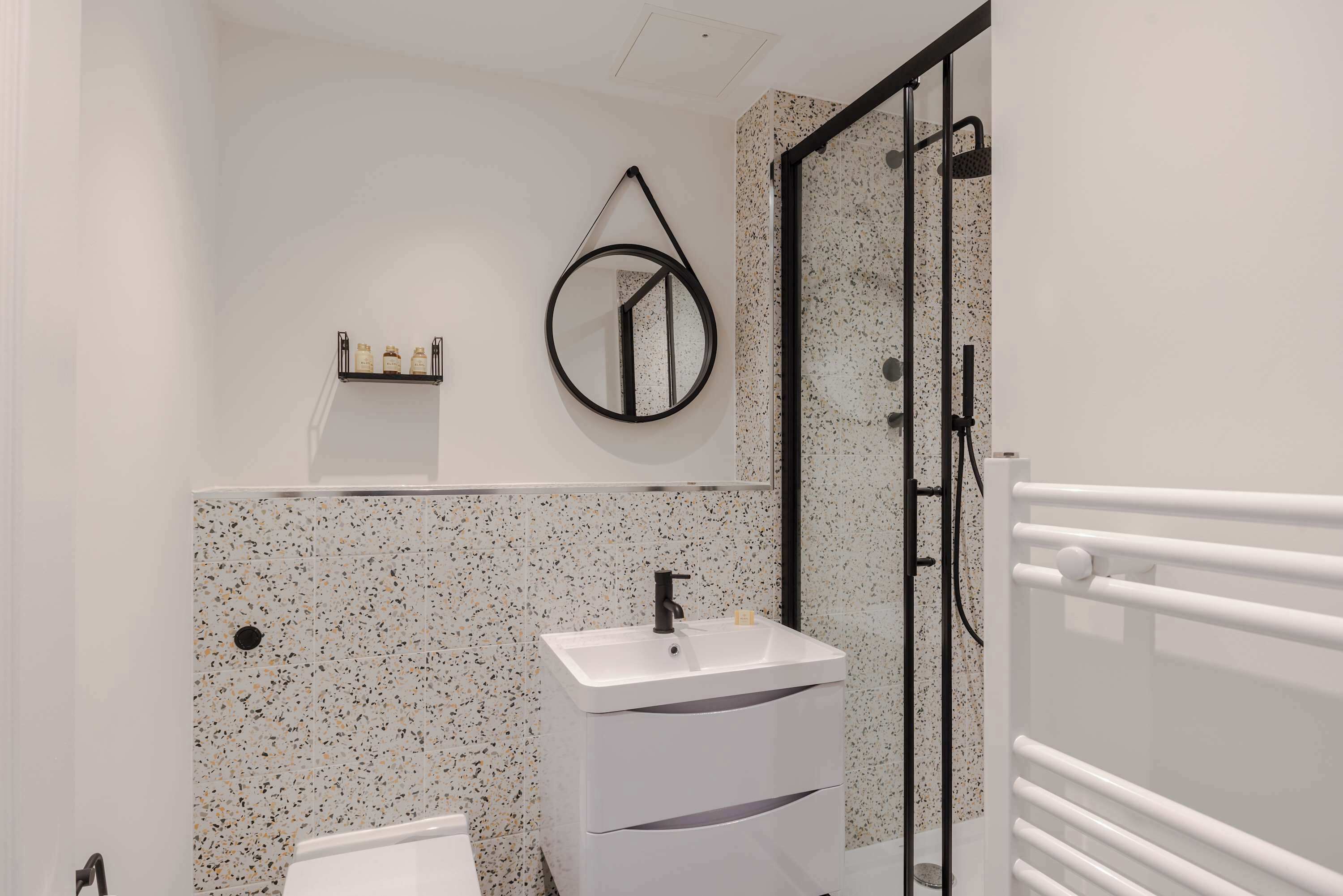Une salle de bain avec un lavabo blanc, un miroir, un porte-serviettes et un espace douche.
