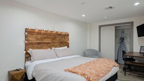 Une chambre d’hôtel moderne avec une tête de lit en bois, un lit avec une literie blanche, une petite table de chevet, un bureau avec une chaise et un téléviseur fixé au mur.