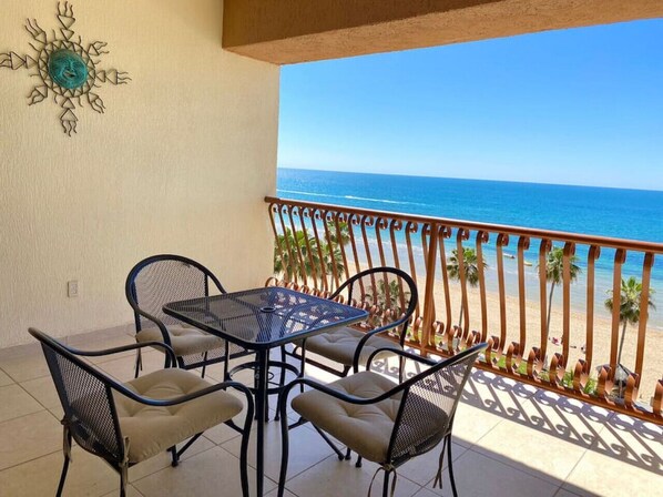 Enjoy ocean views from this balcony with a table and four chairs, surrounded by lush palm trees.