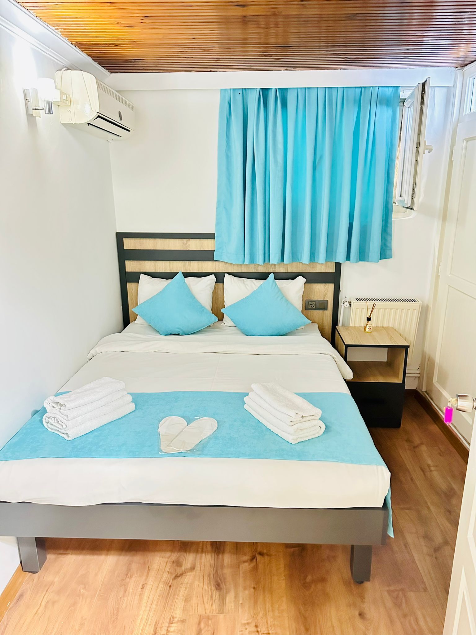 A neatly made bed with blue and white bedding, a wooden headboard, and a blue curtain.