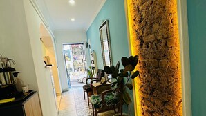 Un pasillo con una zona de cocina a la izquierda, un espacio de descanso con una planta en maceta, y una pared con textura e iluminación cálida a la derecha.
