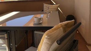 Een balkon met een tafel en stoelen, een witte kop en uitzicht op de bergen.
