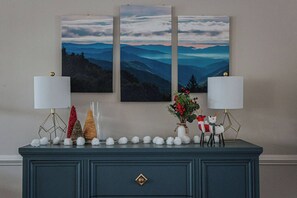 Une commode bleu foncé, ornée de deux lampes, un vase rempli de baies rouges et une décoration représentant un renne.