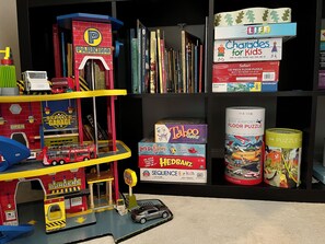 Une bibliothèque contenant divers livres et jeux de société, notamment « The Life of the Party » et « Chardades for Kids ».