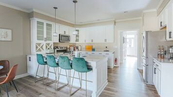 A modern kitchen with white cabinetry, a central island with bar stools, and a dining area with a single chair.