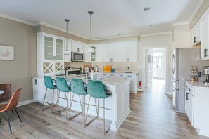 A modern kitchen with white cabinetry, a central island with bar stools, and a dining area with a single chair.