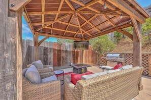 A covered outdoor seating area with wicker furniture, a grill, and a TV. - Monterey Bay Cozy Charmer (Del Rey Oaks)