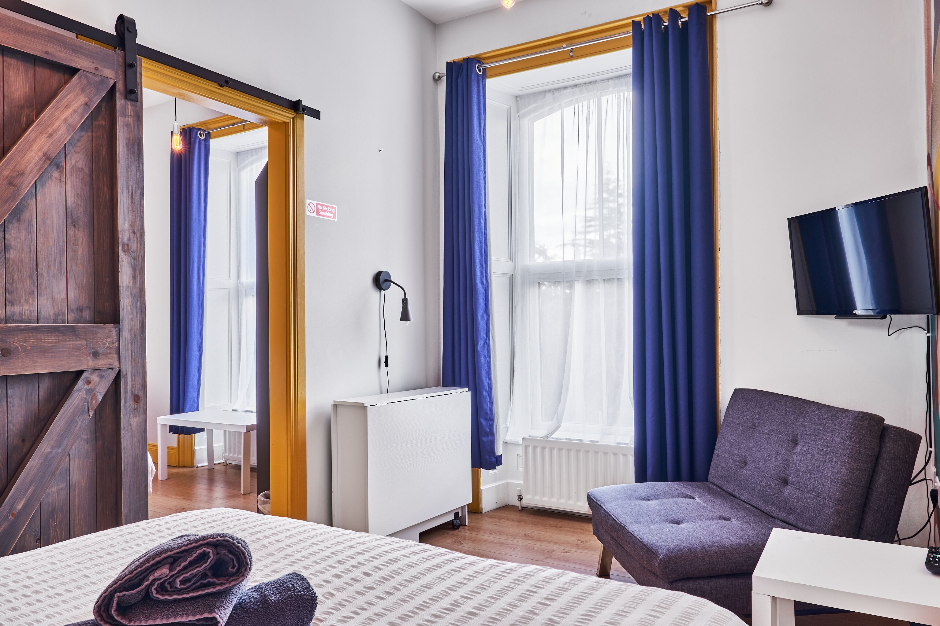 A hotel room with a bed, a sofa, a TV, and a window with curtains.