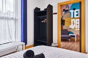 Un dormitorio con cama, armario, banca y ventana con cortinas.